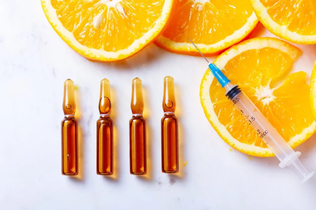 The Power of Vitamin Shots: Fast-Track Your Immunity and Energy This Winter 2 Vitamin C serum ampoules and syringe with fresh orange slices on white marble background