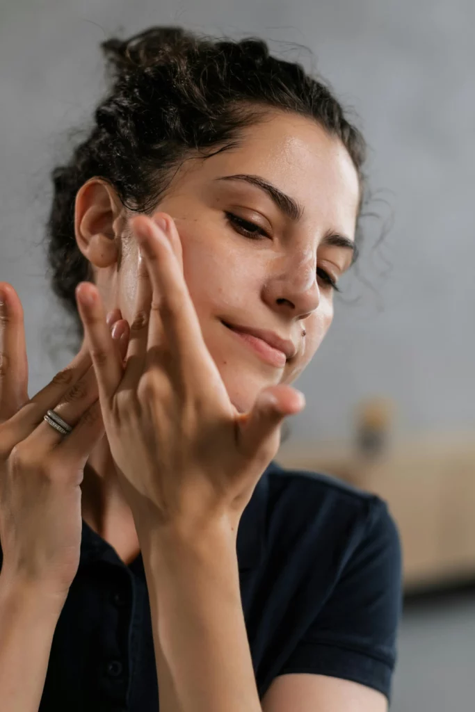 Woman applying facial skincare moisturizer or serum with hands, demonstrating beauty routine and facial care