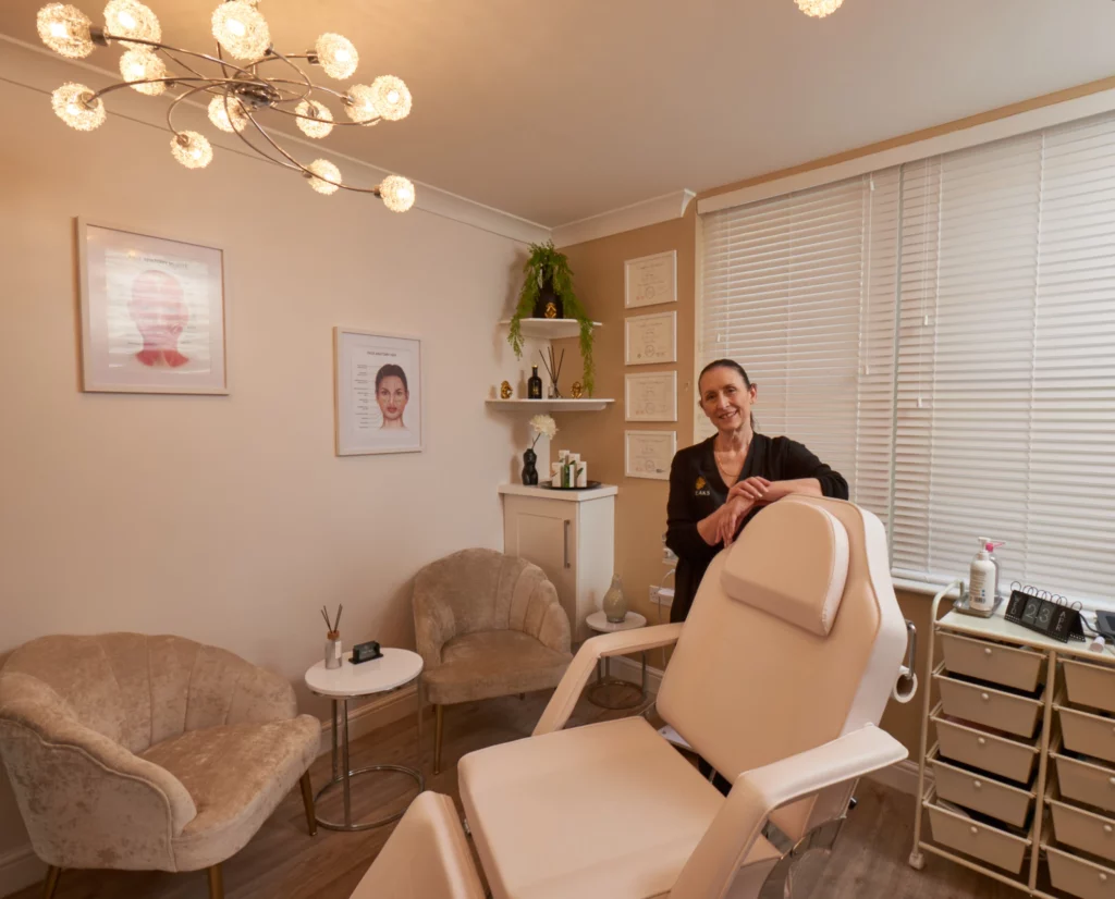 Modern aesthetics treatment room with professional standing beside treatment chair, featuring elegant decor and artistic wall displays